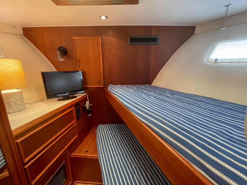 Slide: The Image of 1984 Hatteras 53 Motoryacht cabin with striped bedding, TV, and wooden interior. - 27