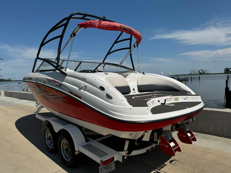 Slide: The Image of 2006 Yamaha Boats AR 210 on trailer by waterfront, featuring sleek design and vibrant red accents. - 1