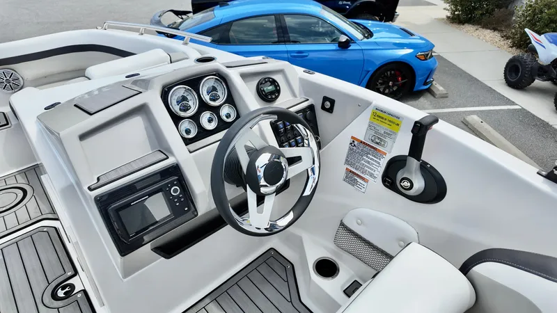 Slide: The Image of 2025 Starcraft SVX 211 IO boat dashboard with steering wheel and gauges, parked near blue car. - 13