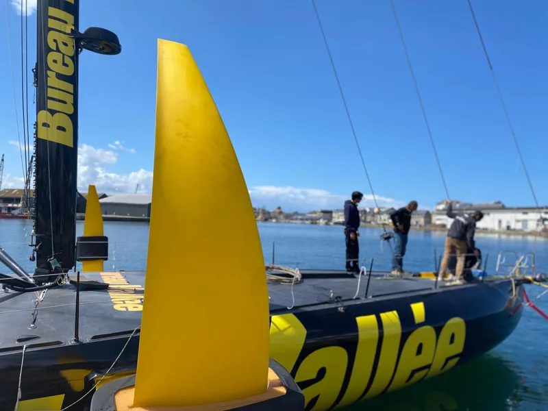 Slide: The Image of Sleek Black Pepper Imoca 2025 sailboat docked, featuring bold yellow accents and crew on deck. - 6