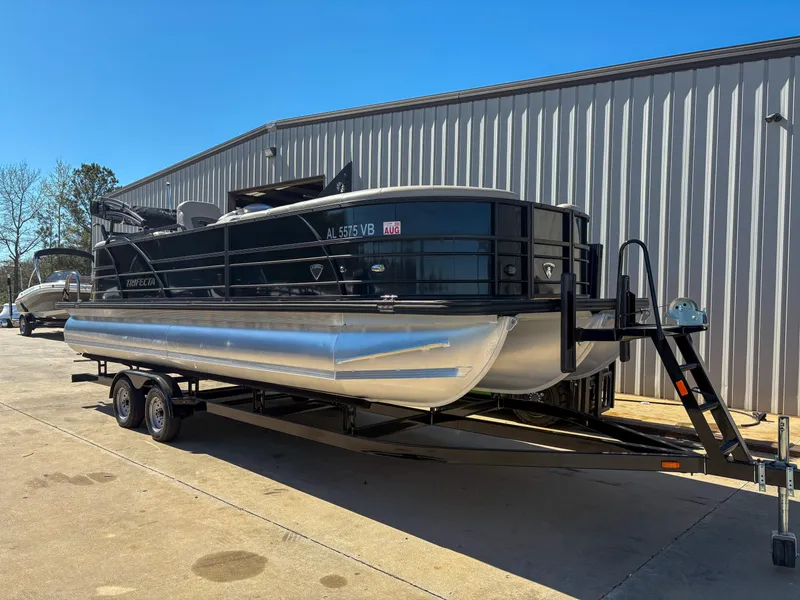 Slide: The Image of 2019 Trifecta 25 RF SS 3.0+ pontoon boat on trailer, parked outside a warehouse. - 0
