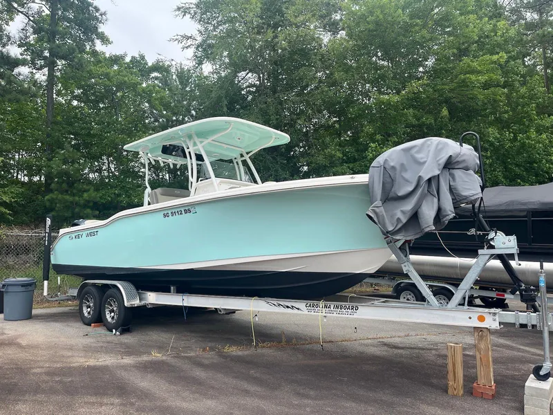 Slide: The Image of 2022 Key West 263 FS boat on trailer, parked outdoors with trees in background. - 0
