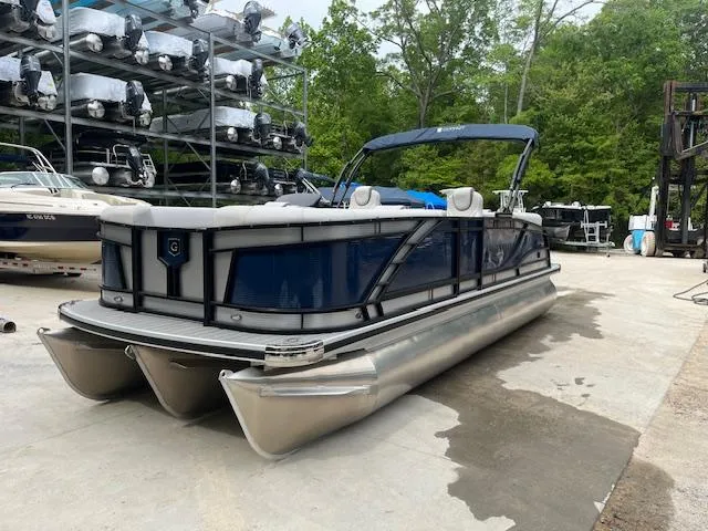 Slide: The Image of 2024 Godfrey Monaco 235 SB pontoon boat in storage, surrounded by trees and other boats. - 2