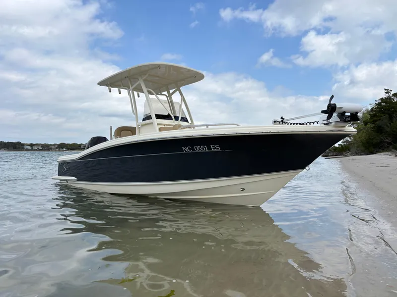 Slide: The Image of 2021 Scout 215XSF boat docked on a sandy shore under a cloudy sky. - 1
