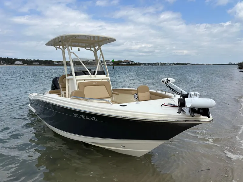 Slide: The Image of 2021 Scout 215XSF boat docked on a sandy shore under a cloudy sky. - 2