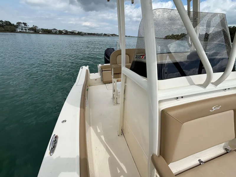 Slide: The Image of 2021 Scout 215XSF boat on calm water, featuring beige seating and a clear windshield. - 24