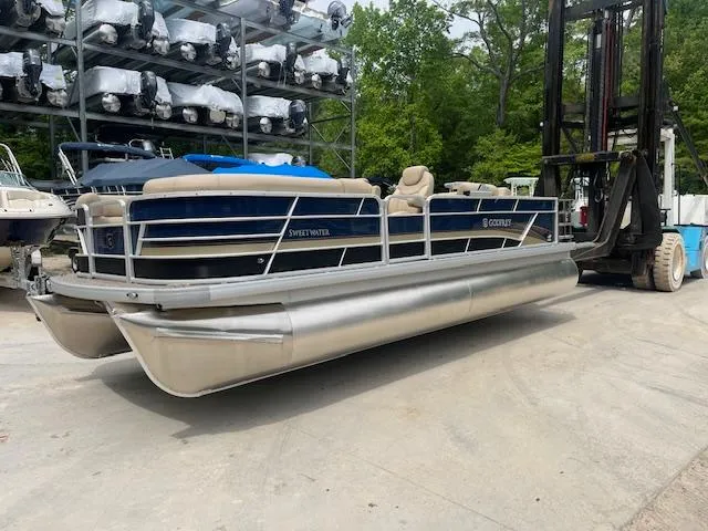 Slide: The Image of 2023 Godfrey SWEETWATER 2286 SFL pontoon boat on forklift, surrounded by trees and stacked boats. - 0