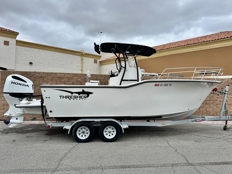 The Image of 2022 Thresher 25 CC boat on trailer with Honda outboard motor, parked outdoors. - 0