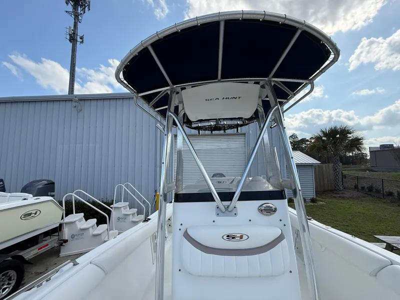 Slide: The Image of 2010 Sea Hunt Ultra 210 boat with T-top, docked near a metal building under a blue sky. - 43