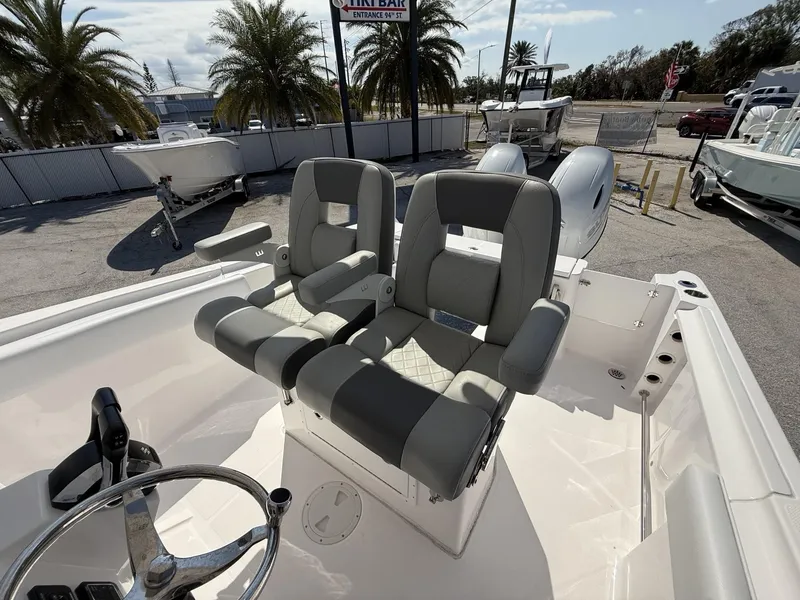 Slide: The Image of 2024 Aquasport 2500 CC boat with dual captain's chairs and steering wheel, parked outdoors. - 19