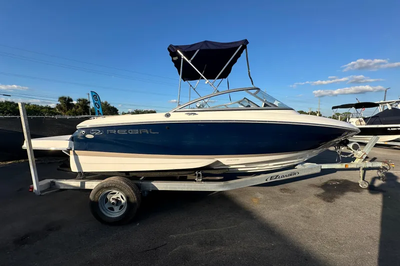 Slide: The Image of 2017 Regal 1900 Bowrider boat on trailer, blue and white design, sunny day. - 1