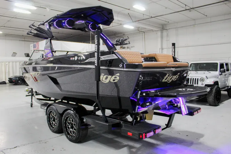 Slide: The Image of 2025 Tigé 22RZX boat on trailer in showroom with purple lighting. - 2