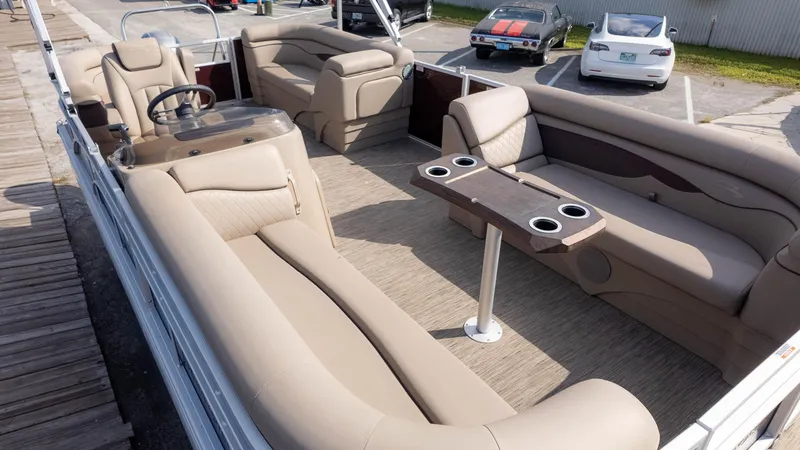 Slide: The Image of 2024 Bennington 20SSR pontoon boat with beige seating and cup holders, docked near parked cars. - 4