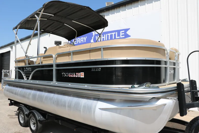 Slide: The Image of 2019 Lowe SS210 pontoon boat with canopy on a trailer, parked outside a building. - 10
