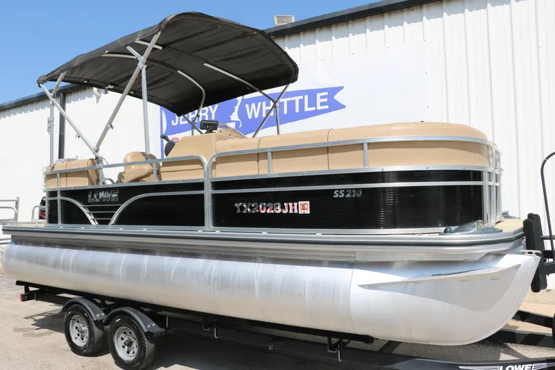 Slide: The Image of 2019 Lowe SS210 pontoon boat with canopy on trailer, parked outside a building. - 11