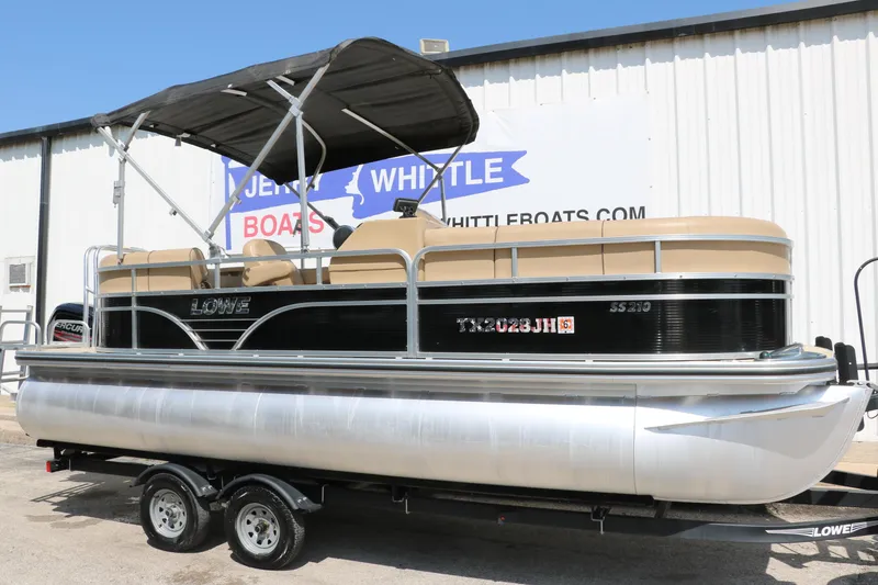 Slide: The Image of 2019 Lowe SS210 pontoon boat with canopy on trailer, parked outside a building. - 12