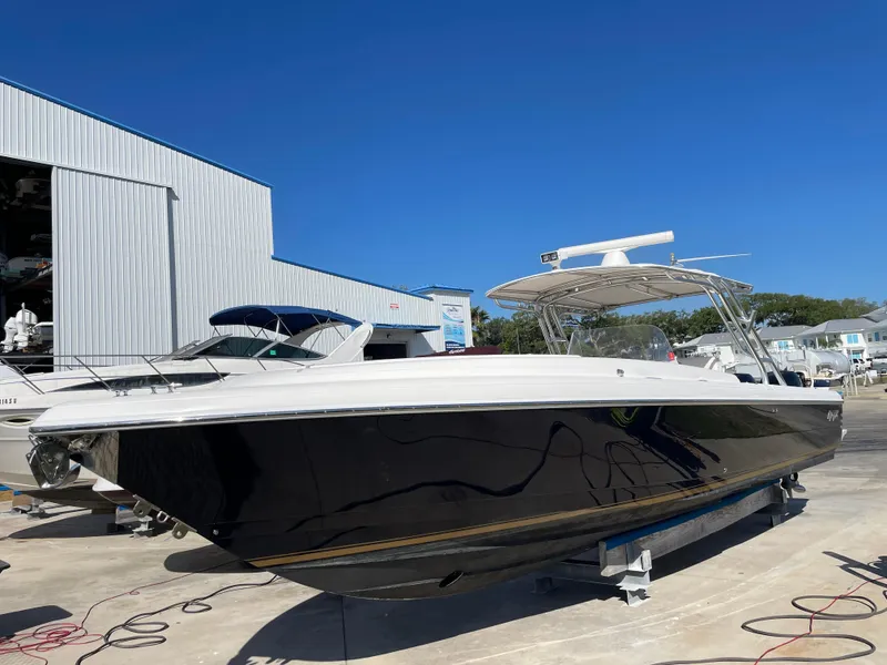 Slide: The Image of 2008 Intrepid 323 Cuddy boat with sleek black hull, docked outdoors under clear blue sky. - 2