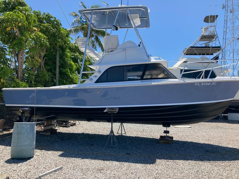 Slide: The Image of 1974 Bertram 31 Flybridge Cruiser on dry dock, surrounded by trees and other boats. - 12