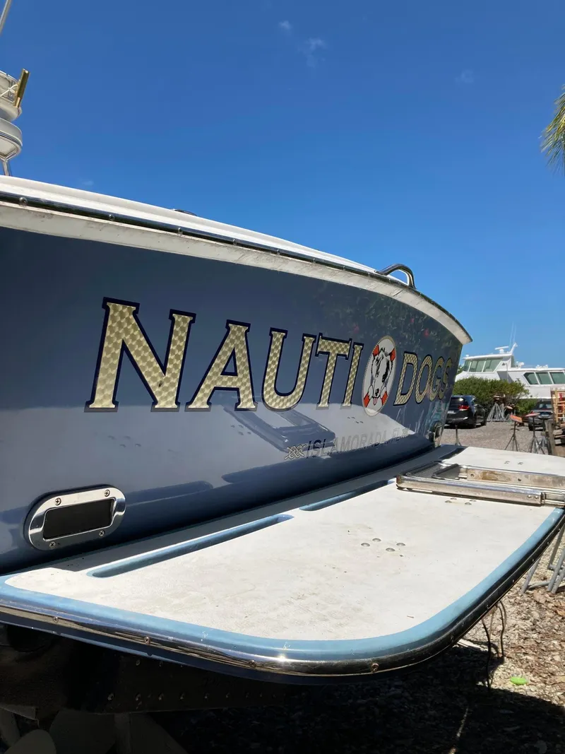 Slide: The Image of 1974 Bertram 31 Flybridge Cruiser with "Nauti Dog" name, docked under clear blue sky. - 19