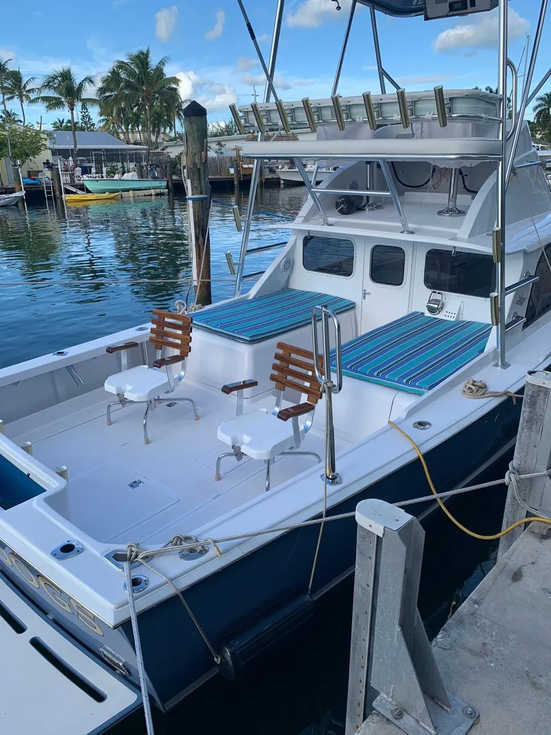 Slide: The Image of 1974 Bertram 31 Flybridge Cruiser docked, featuring spacious deck and seating, under clear skies. - 3