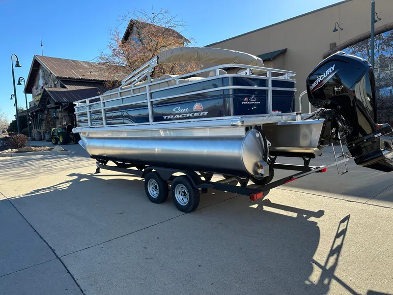 Slide: The Image of 2025 Sun Tracker Fishin' Barge 20 DLX pontoon boat on trailer, outdoor setting. - 2