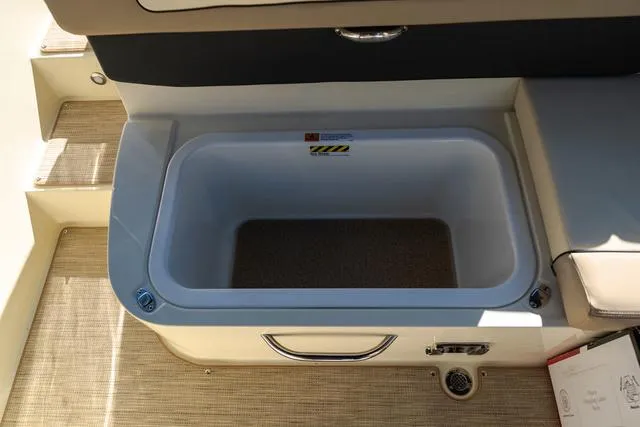 Slide: The Image of 2025 Chris-Craft 25 Sportster boat storage compartment with beige interior and handle. - 11