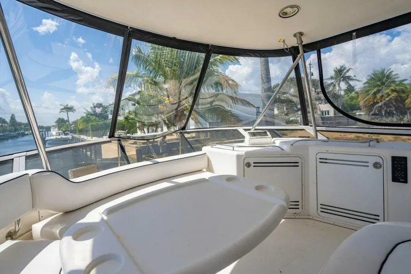 Slide: The Image of 1999 Sea Ray 56 Sedan Bridge interior with panoramic windows and seating, overlooking a tropical waterfront. - 31