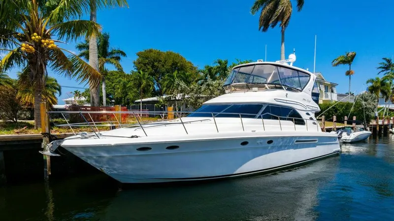 Slide: The Image of 1999 Sea Ray 56 Sedan Bridge yacht docked by palm trees, under clear blue sky. - 5