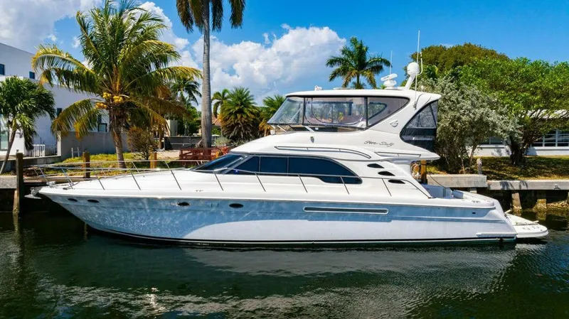 Slide: The Image of 1999 Sea Ray 56 Sedan Bridge yacht docked by palm trees, under a clear blue sky. - 6