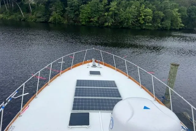 Slide: The Image of 1980 Huckins Sports Cruiser with solar panels on deck, cruising on a serene river. - 8