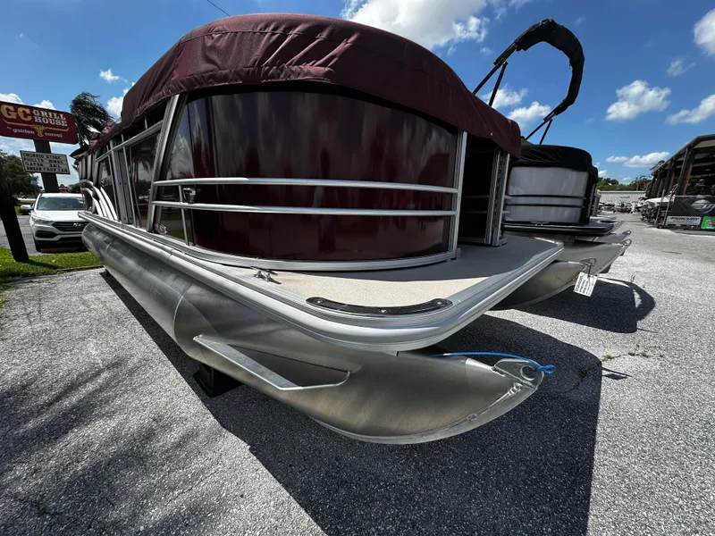 Slide: The Image of 2025 Sylvan Mirage 820 Cruise pontoon boat with maroon canopy, parked on gravel. - 2