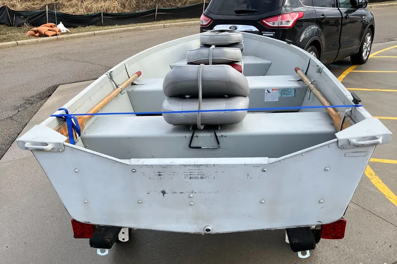 Slide: The Image of 2001 Alumacraft T12V boat on trailer, parked in a lot, with oars and seats visible. - 2