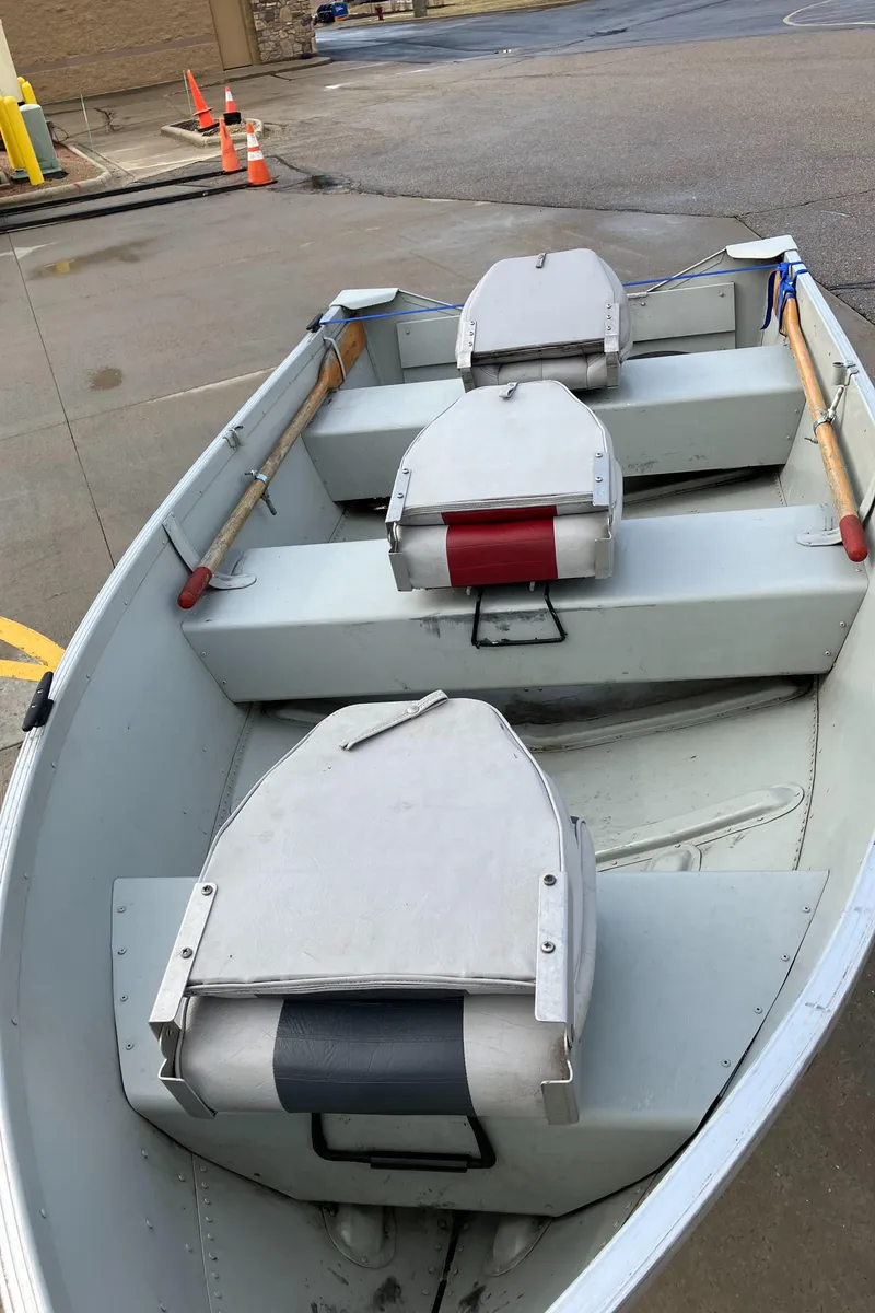 Slide: The Image of 2001 Alumacraft T12V boat with three seats and wooden oars, parked on concrete. - 4