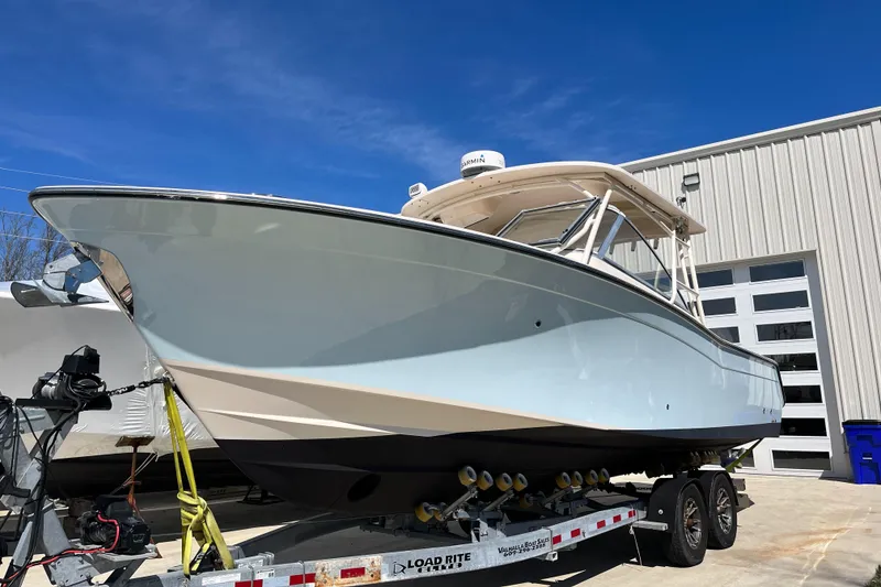 Slide: The Image of 2013 Grady-White Freedom 307 boat on trailer, parked outside a building under clear blue sky. - 2