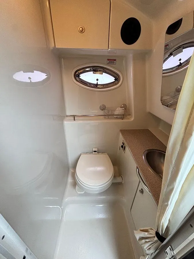 Slide: The Image of 2006 Sea Ray 290 Sundancer bathroom with toilet, sink, and porthole window. - 24