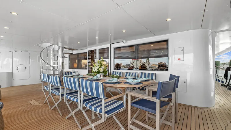 Slide: The Image of Outdoor dining area on 2005 New Zealand Yachts Wave Piercer, featuring striped chairs and wooden table. - 19