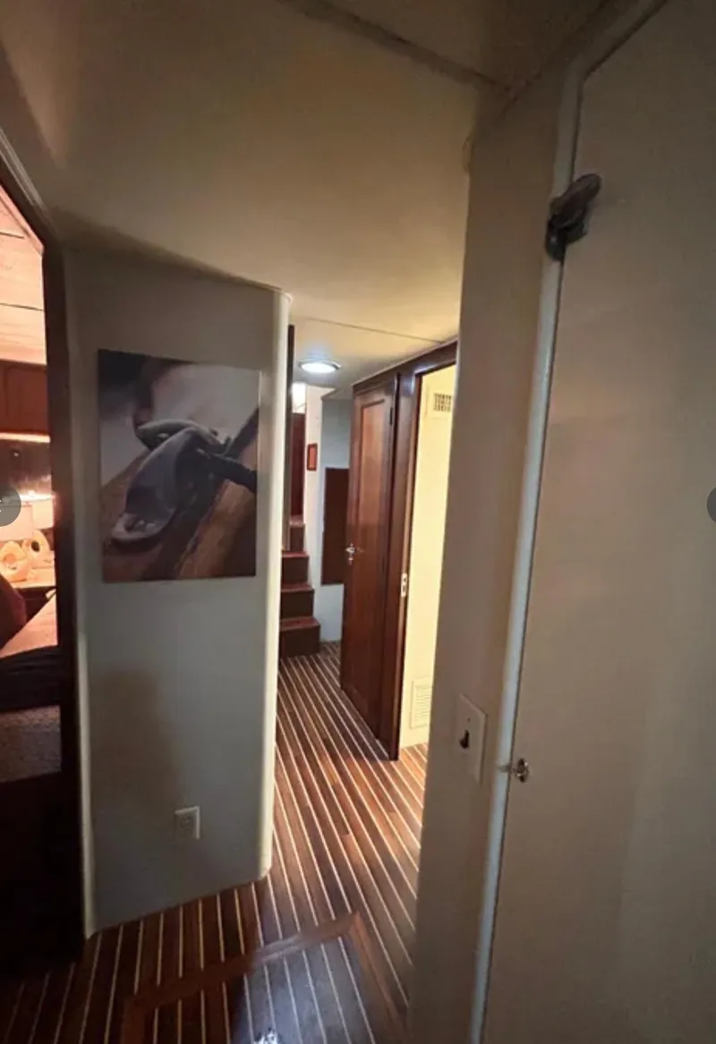 Slide: The Image of Hallway inside 1989 Hatteras 67 Cockpit Motor Yacht with wooden flooring and artwork. - 23