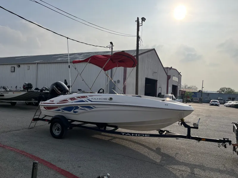 Slide: The Image of 2022 Tahoe T16 boat with red canopy on trailer, parked outdoors near warehouse. - 37
