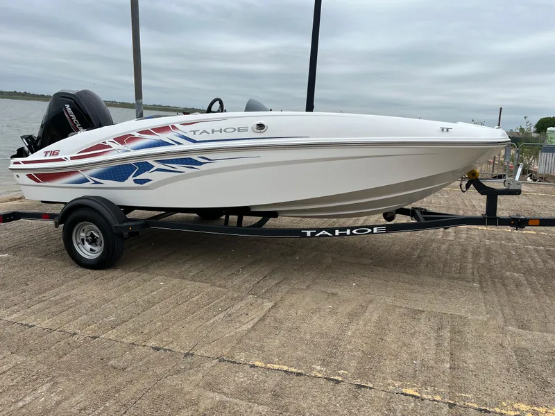 Slide: The Image of 2022 Tahoe T16 boat on trailer, white with red and blue graphics, parked on concrete. - 40