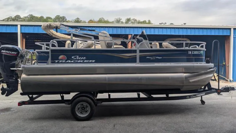 Slide: The Image of 2024 Sun Tracker Bass Buggy 18 DLX pontoon boat on trailer, parked outdoors. - 3