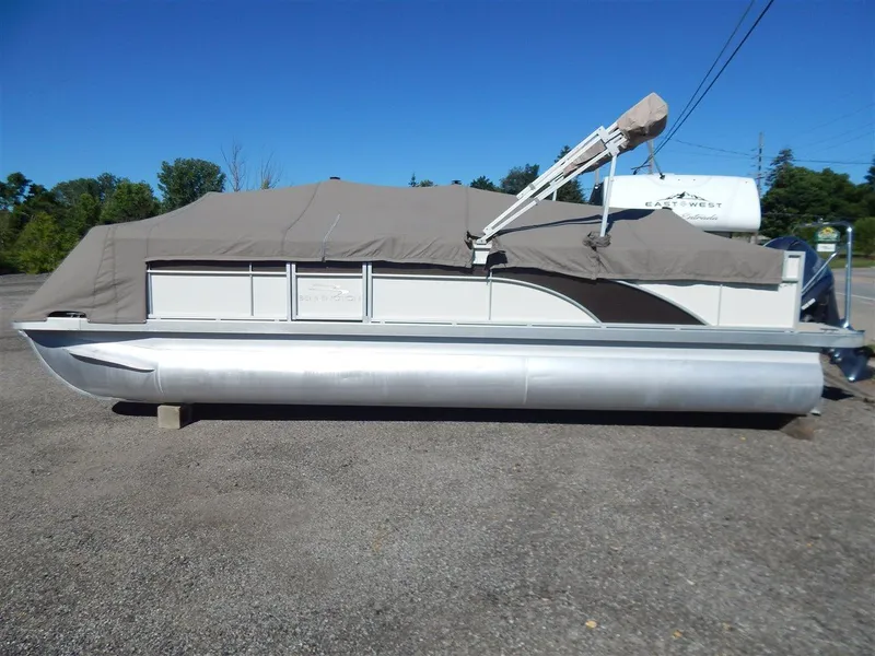 Slide: The Image of 2016 Bennington 24 SSLX pontoon boat covered, parked on gravel lot. - 1