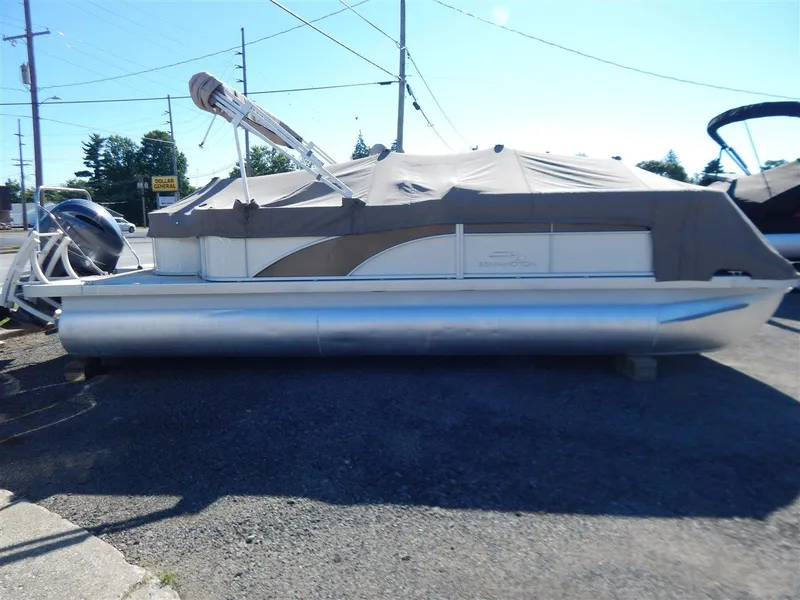 Slide: The Image of 2016 Bennington 24 SSLX pontoon boat with cover, parked on gravel lot. - 2