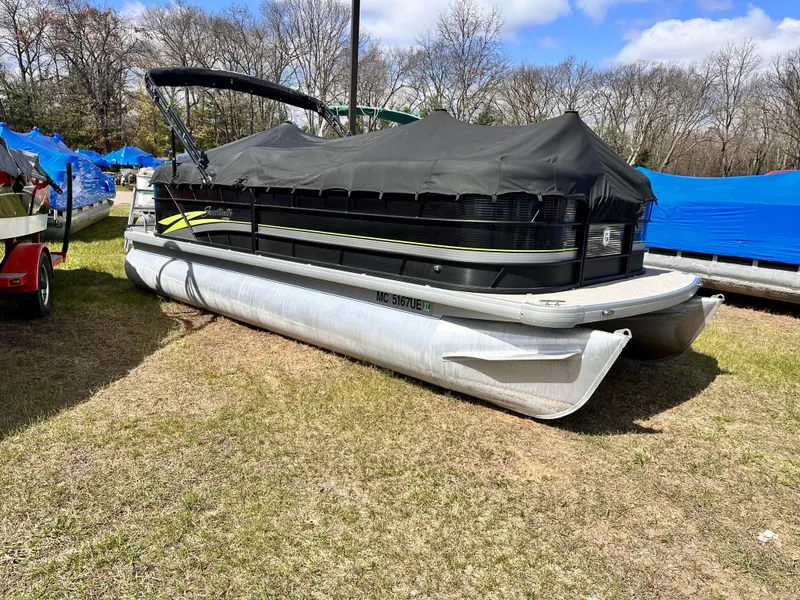 Slide: The Image of 2018 Sweetwater 2286 pontoon boat covered, parked on grass, surrounded by trees and other boats. - 1