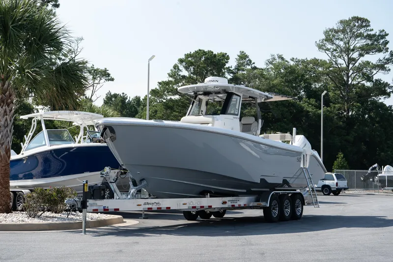 Slide: The Image of 2025 Solace 32 CS boat on trailer, parked outdoors near trees and other boats. - 11