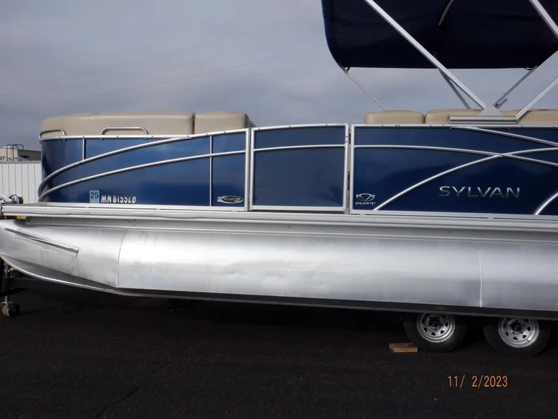 Slide: The Image of 2013 Sylvan Signature 8523 LZ pontoon boat with blue and silver design on trailer. - 16