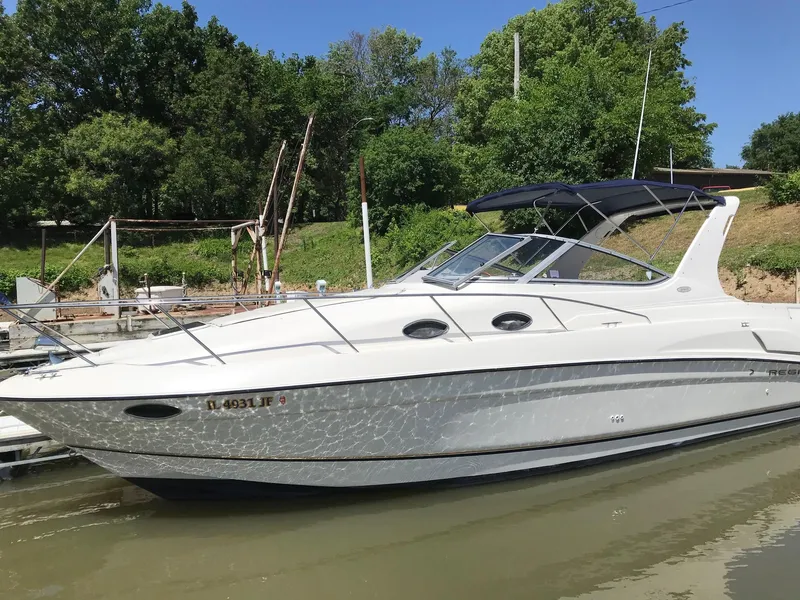 Slide: The Image of 1999 Regal 292 Commodore boat docked on a sunny day, surrounded by lush greenery. - 0