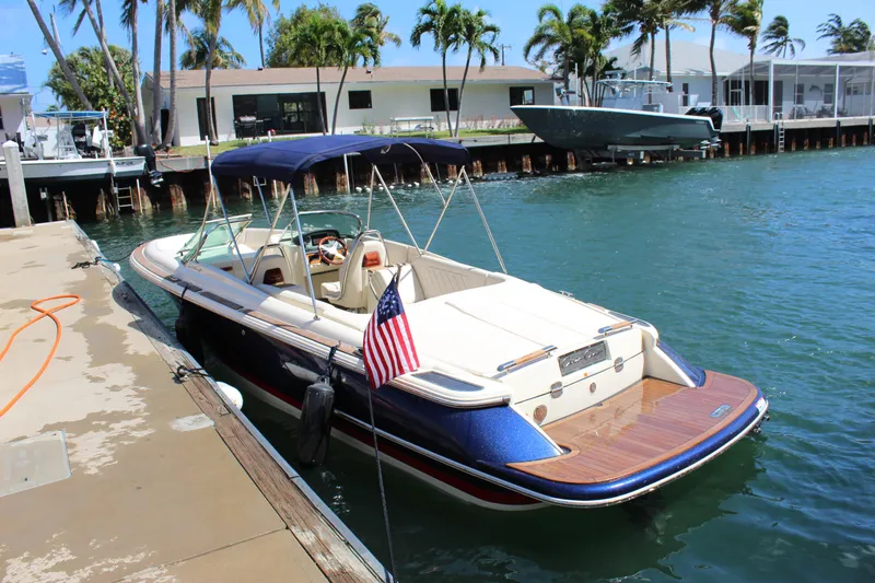 Slide: The Image of 2022 Chris-Craft Launch 27 boat docked by waterfront with American flag. - 29