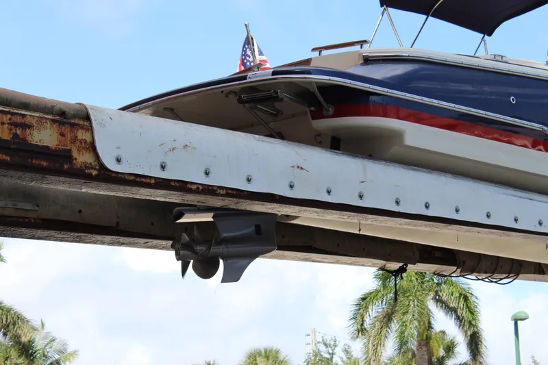 Slide: The Image of 2022 Chris-Craft Launch 27 boat on lift, showcasing hull and propeller, with palm trees in background. - 37