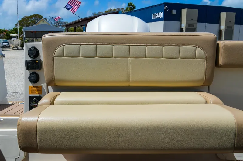Slide: The Image of 2019 Sailfish 245 DC boat seat with beige upholstery, outdoor setting, American flag in background. - 16