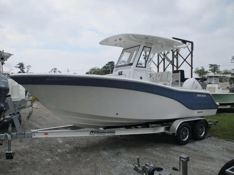 Slide: The Image of 2025 Sea Fox 228 Commander boat on trailer, white and blue design, parked outdoors. - 0